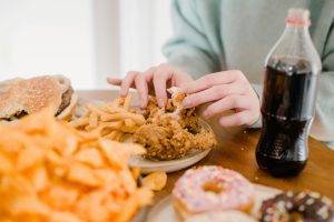Crop anonymous female eating appetizing spicy fried chicked at table with different snacks